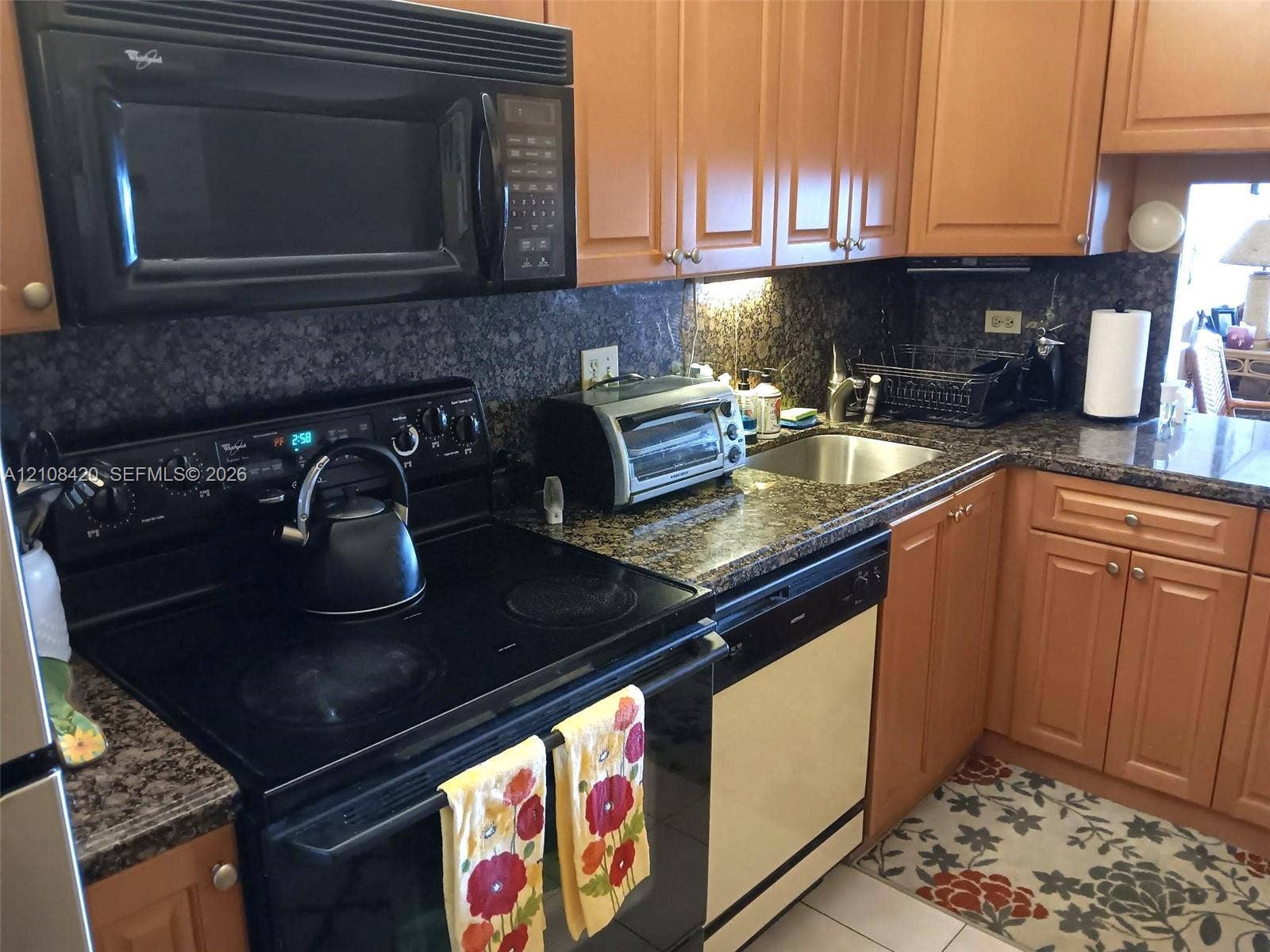 3545 NE 166th Street, #306, North Miami Beach, FL 33160 Kitchen featuring medium-tone wood cabinetry, dark stone countertops, an integrated over-the-range microwave, a smooth-top electric range, and a stainless steel undermount sink
