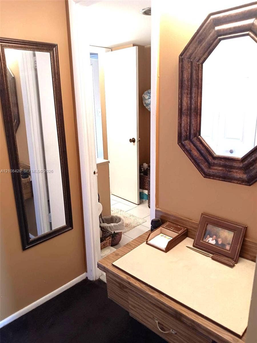 3545 NE 166th Street, #306, North Miami Beach, FL 33160 Built-in wood vanity featuring a flat-surface countertop, an octagonal wall-mounted mirror, and a full-length rectangular wall-mounted mirror