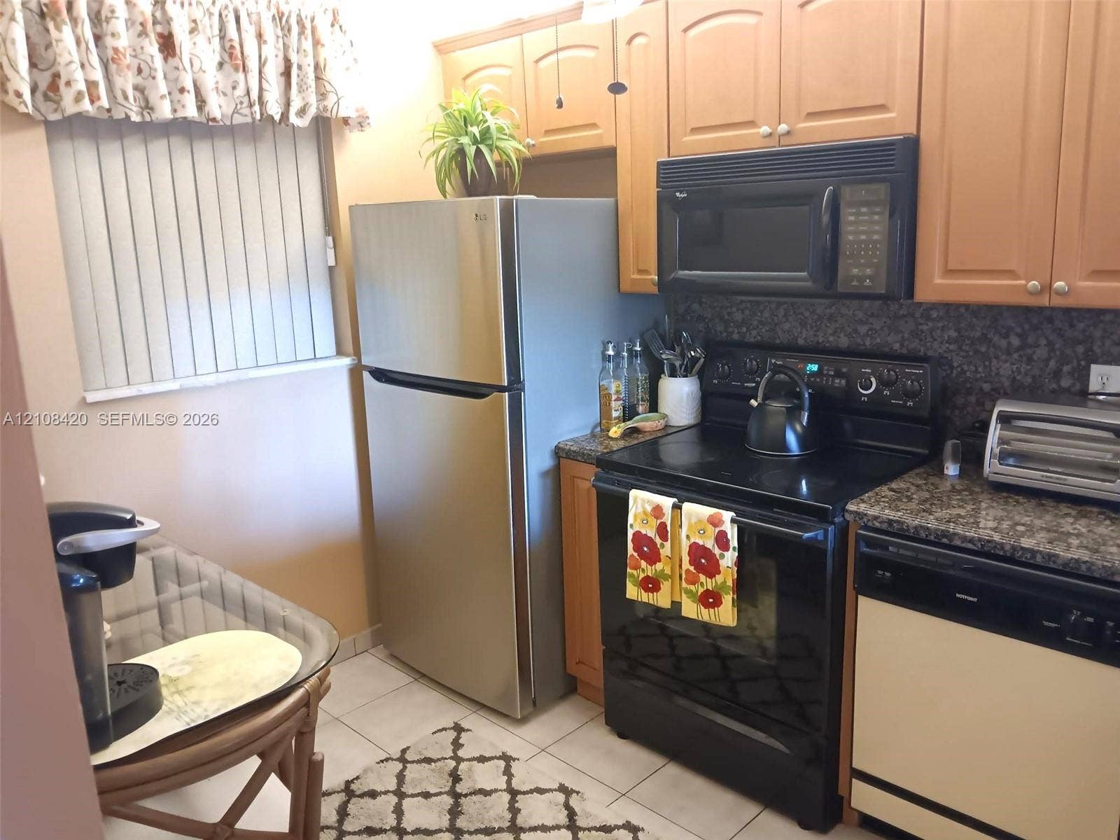 3545 NE 166th Street, #306, North Miami Beach, FL 33160 Kitchen featuring natural wood-finish cabinetry, stone-texture countertops, tile flooring, and integrated black appliances