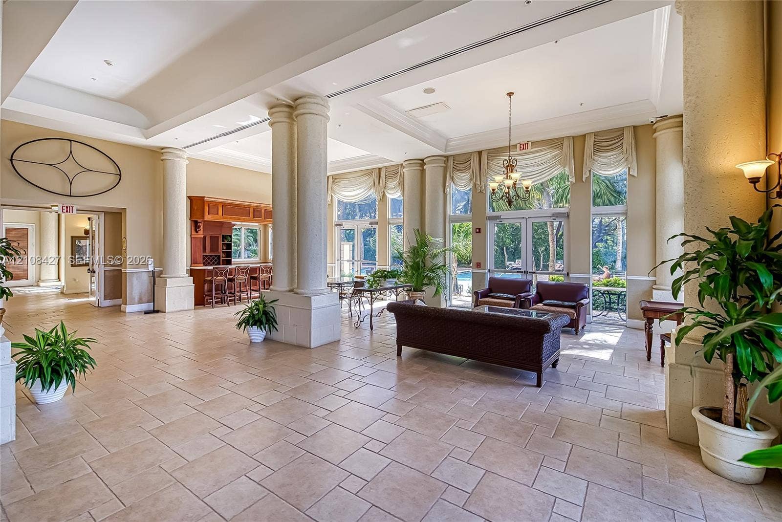 Open-concept common area featuring ceramic tile flooring, soaring tray ceilings, structural columns, built-in wooden bar cabinetry, and floor-to-ceiling glass panel doors