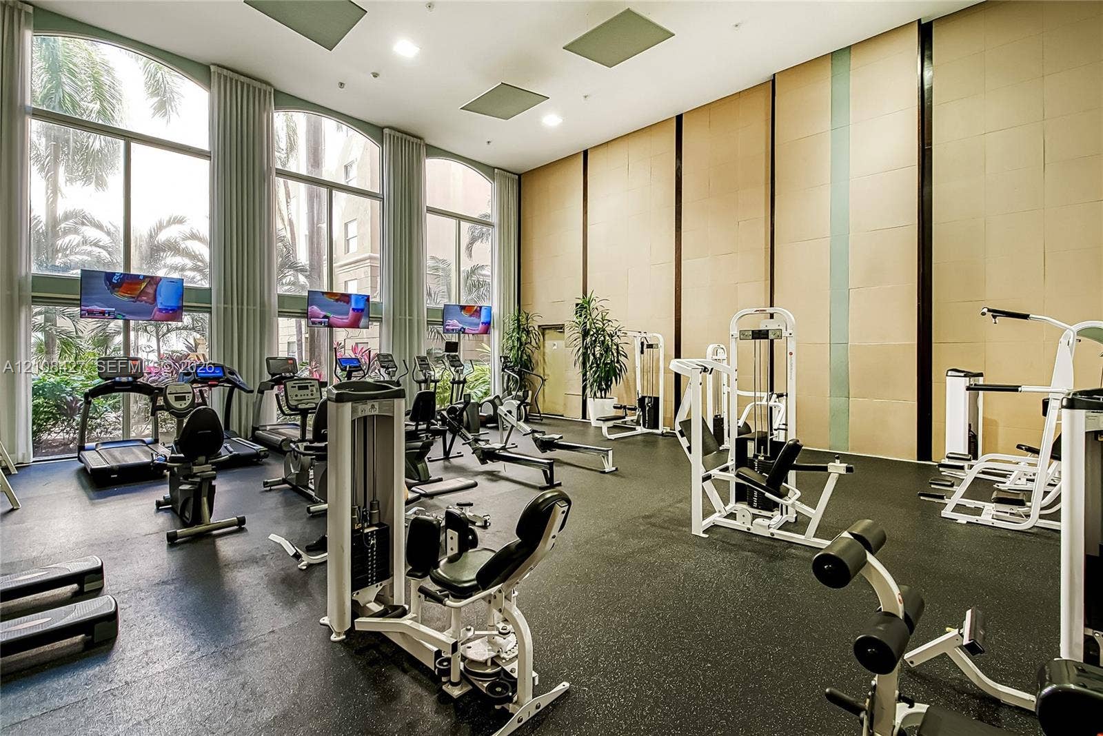 Fitness center featuring double-height ceilings, floor-to-ceiling arched windows, recessed lighting, and wall paneling