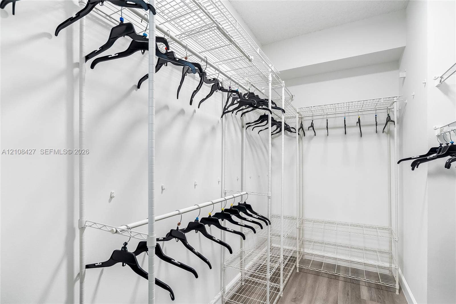 Walk-in closet featuring floor-to-ceiling white wire shelving systems and wood-finish flooring