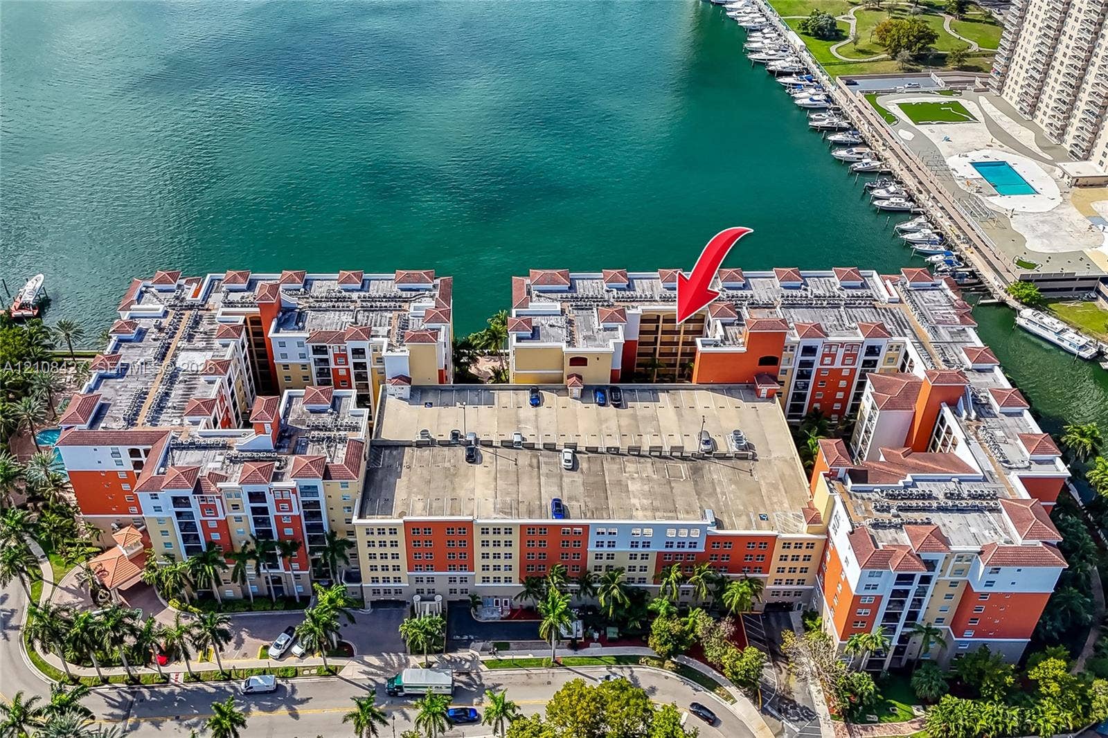 Aerial perspective of a multi-story residential complex featuring tile roofing, stucco exterior, integrated parking structure, and direct waterfront access
