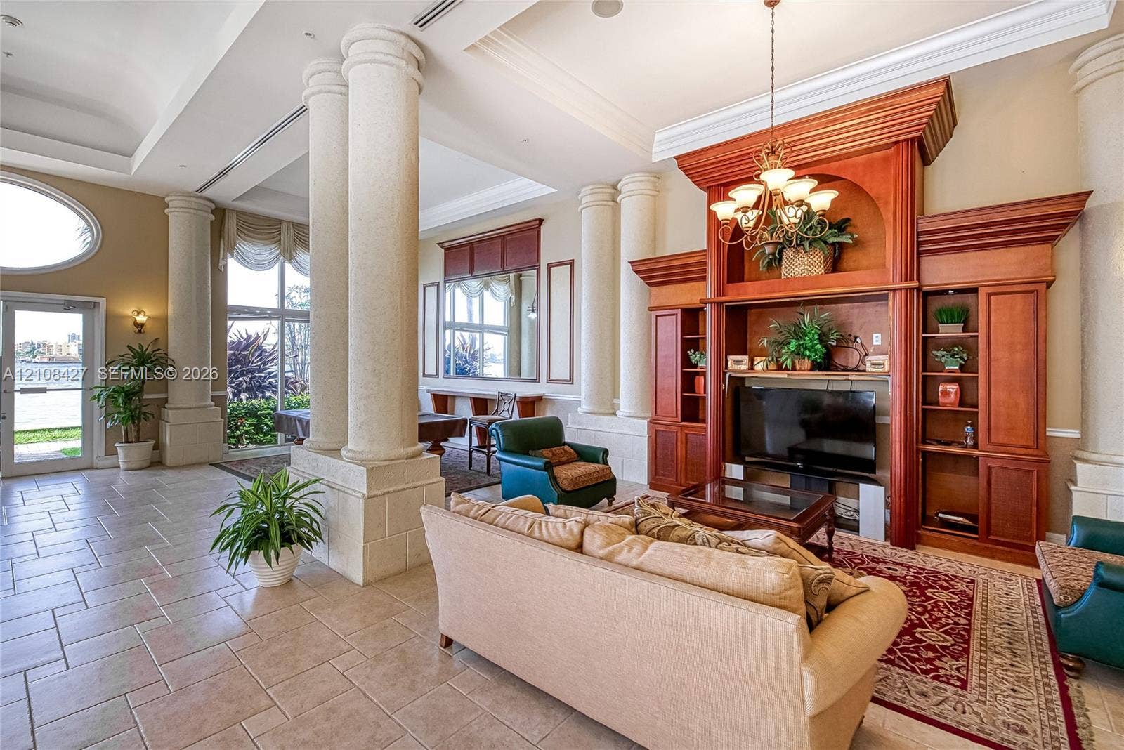 Grand hall featuring soaring ceilings, oversized structural columns, large-scale tile flooring, and custom built-in wood cabinetry with integrated shelving