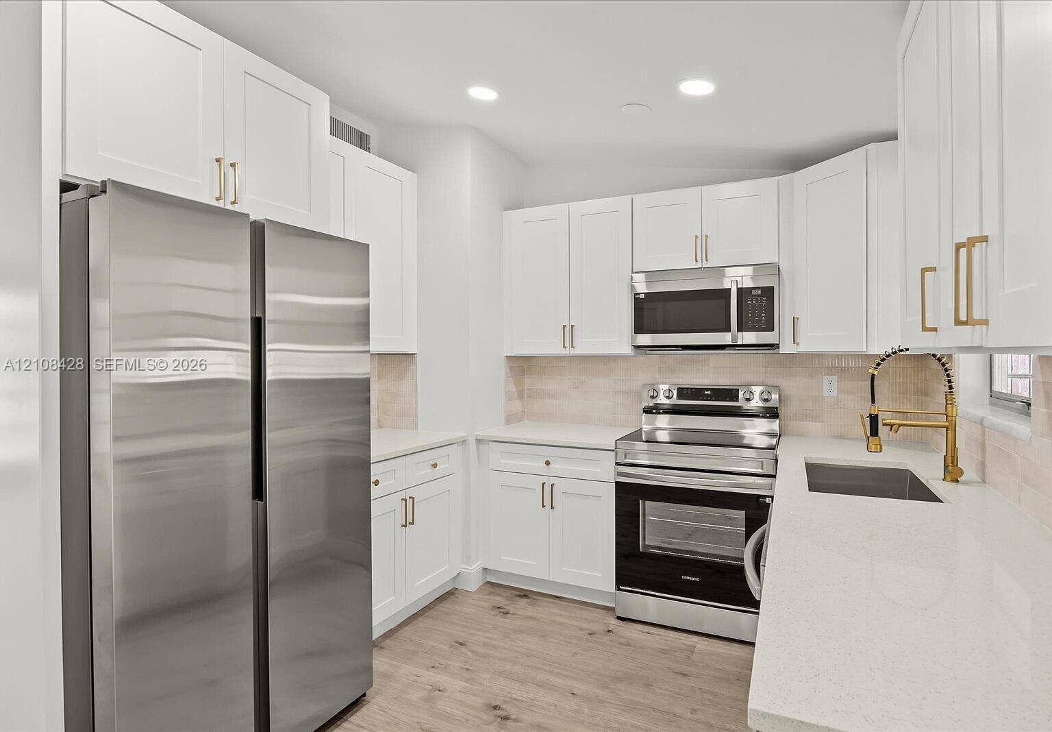 555 SE Airoso Boulevard, Port St Lucie, Port St Lucie, FL 34983 Kitchen featuring white shaker-style cabinetry with gold-tone hardware, stone countertops, stainless steel appliances, wood-finish flooring, and a gooseneck faucet