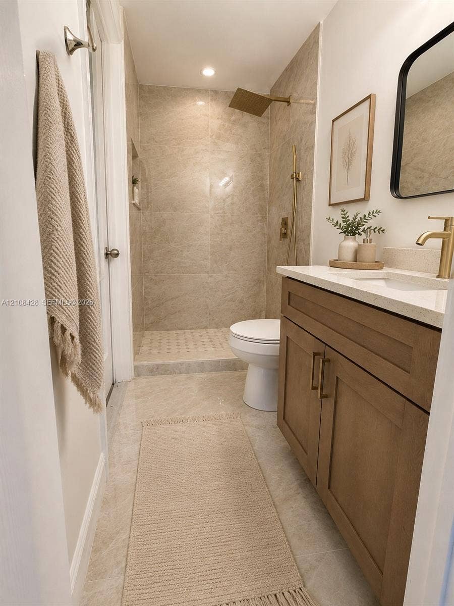 555 SE Airoso Boulevard, Port St Lucie, Port St Lucie, FL 34983 Bathroom featuring a wood-finish vanity with a light-toned countertop, brass-toned hardware, a walk-in shower with stone-style tile, and a rainfall showerhead