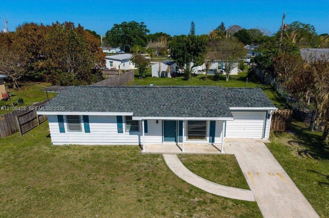 555 SE Airoso Boulevard, Port St Lucie, Port St Lucie, FL 34983 Single-story residence featuring white horizontal siding, a pitched asphalt shingle roof, blue window shutters, a concrete driveway, and an attached one-car garage