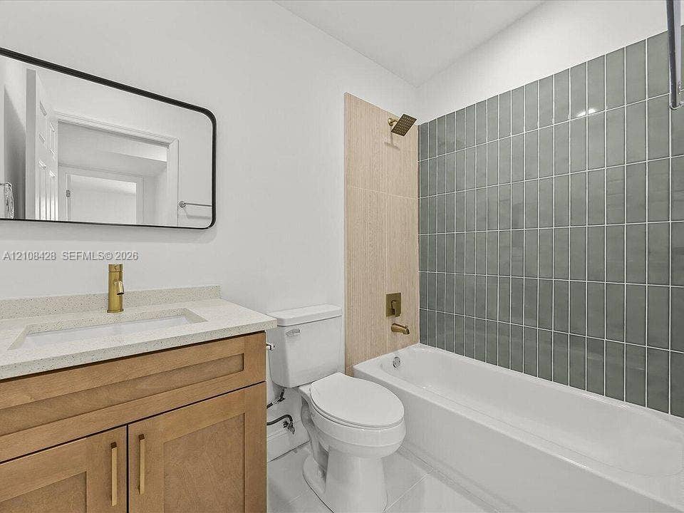 555 SE Airoso Boulevard, Port St Lucie, Port St Lucie, FL 34983 Bathroom featuring a wood-finish vanity with a stone-composite countertop, rectangular undermount sink, brass-finish fixtures, and a glass-tiled shower surround
