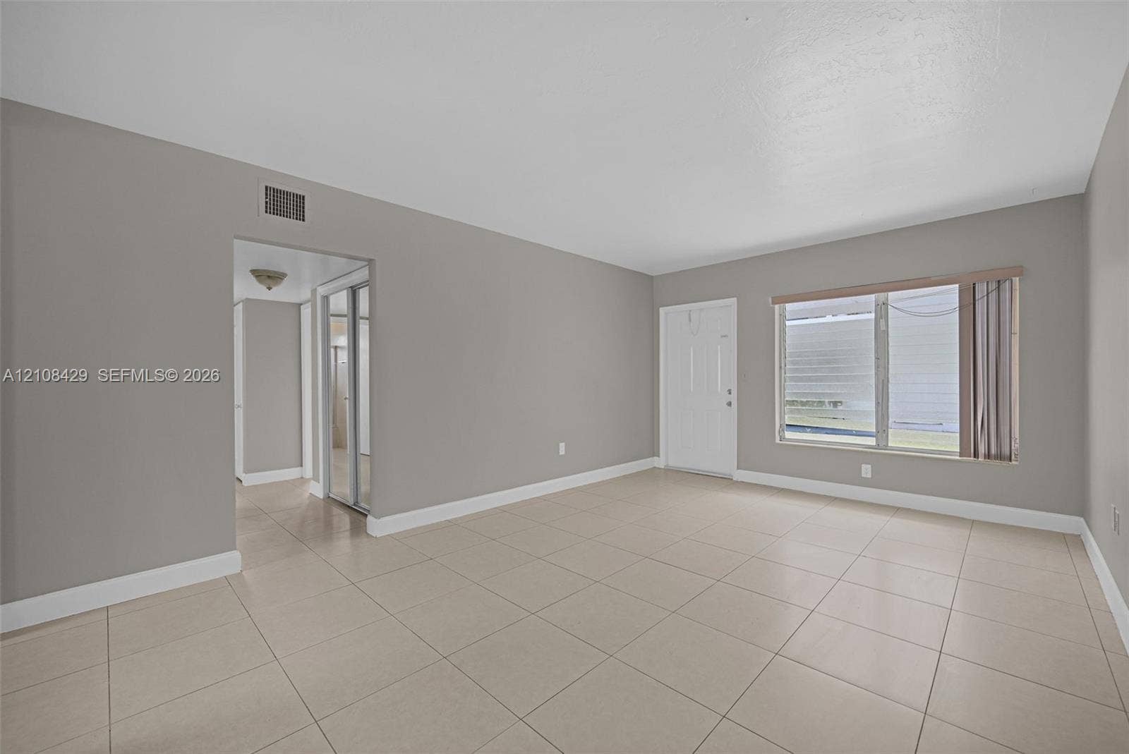 1430 NE 171st Street, North Miami Beach, FL 33162 Neutral-toned interior featuring large-format ceramic tile flooring, neutral wall paint, and a wide window with a horizontal blind