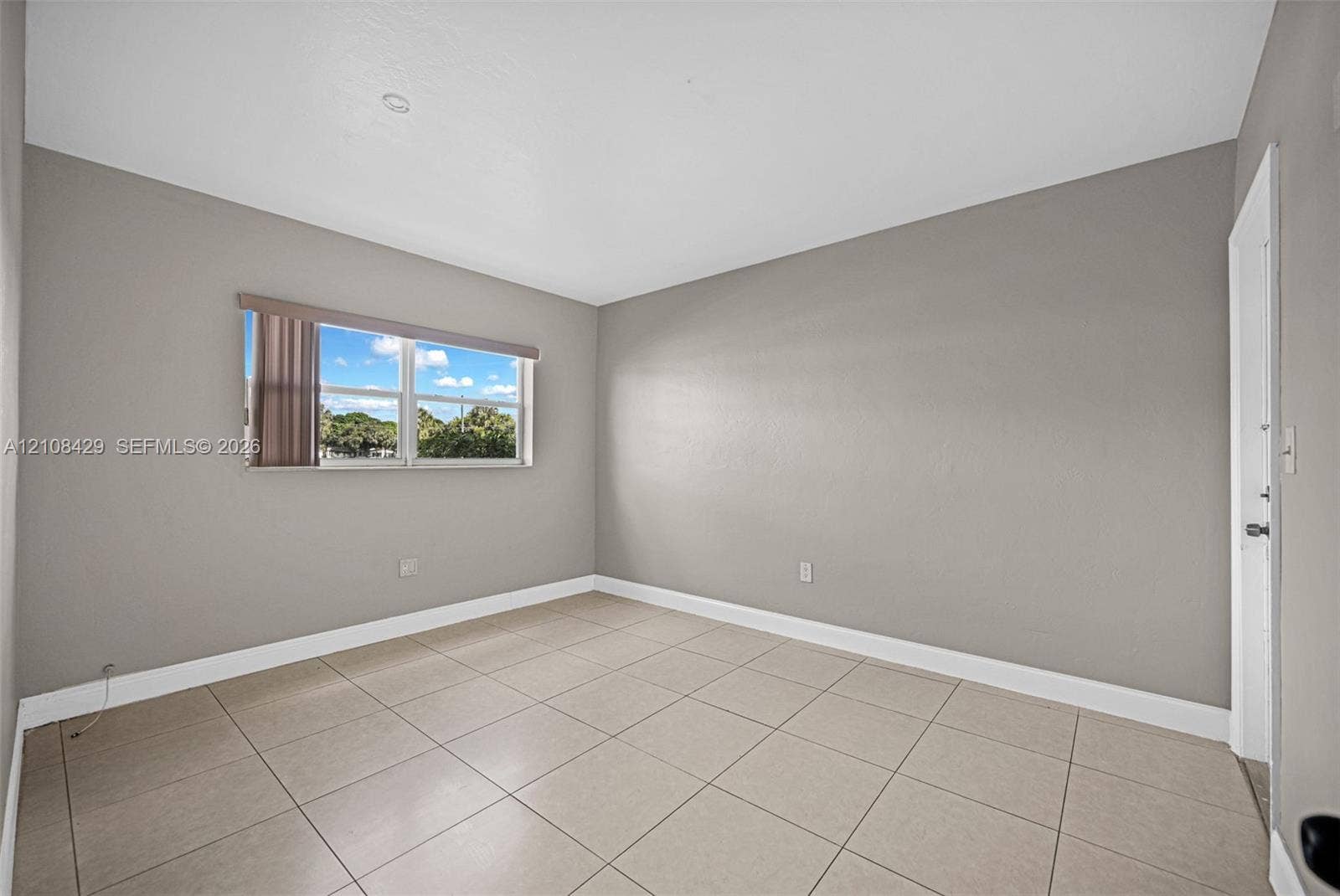 1430 NE 171st Street, North Miami Beach, FL 33162 Neutral-toned interior space featuring light-colored ceramic tile flooring, smooth walls, and a window with horizontal blinds
