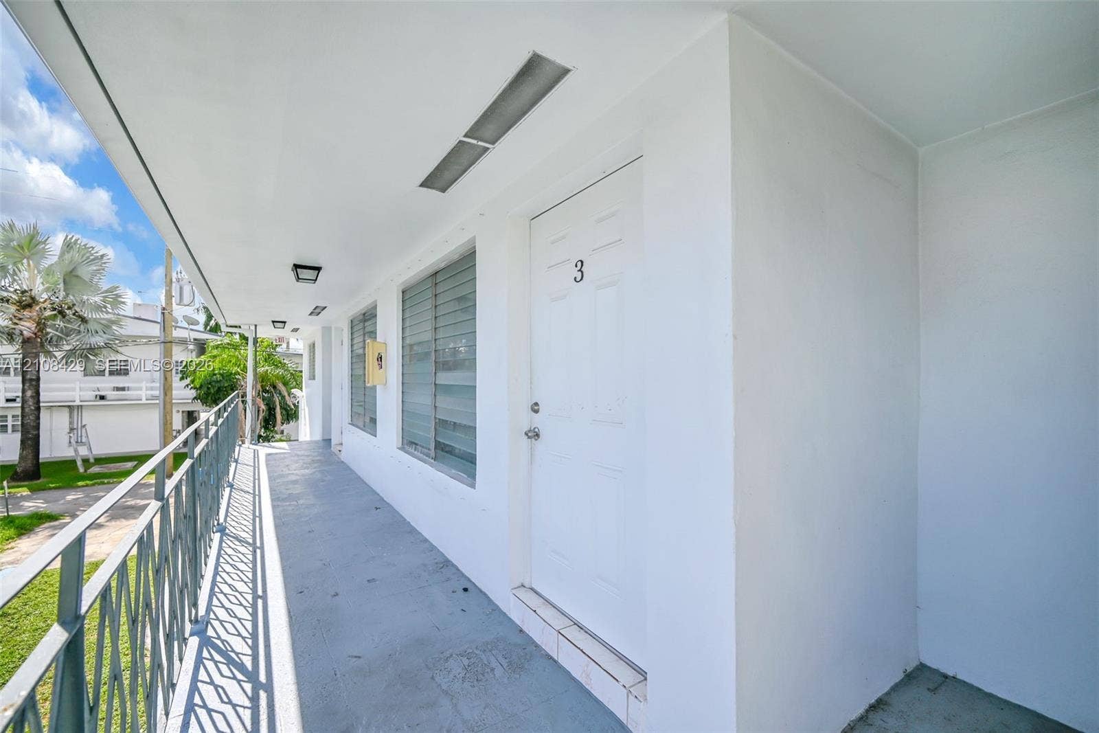 1430 NE 171st Street, North Miami Beach, FL 33162 Covered exterior walkway featuring metal railings, horizontal-slatted windows, and recessed ceiling lighting