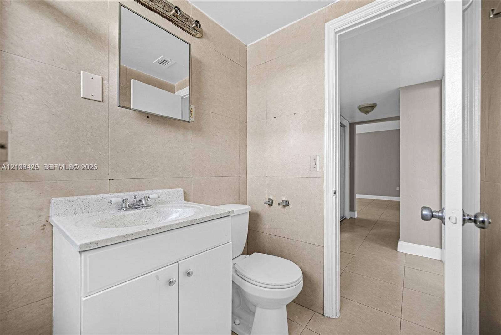 1430 NE 171st Street, North Miami Beach, FL 33162 Bathroom featuring large-format wall tiling, white vanity with a solid surface countertop, rectangular under-mount sink, and chrome fixtures