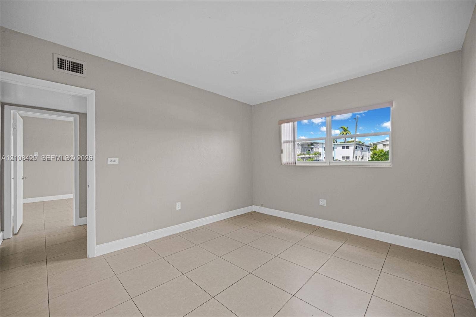 1430 NE 171st Street, North Miami Beach, FL 33162 Neutral-toned interior space featuring light-colored tile flooring, smooth walls, and a large window with horizontal blinds