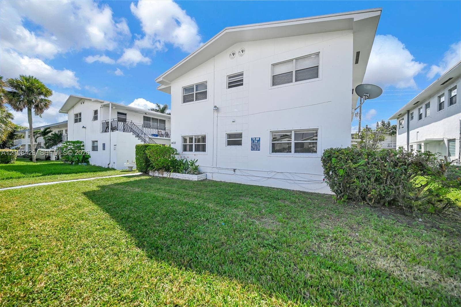 1430 NE 171st Street, North Miami Beach, FL 33162 Multi-story exterior featuring white stucco siding, a low-pitch roofline, and manicured green space