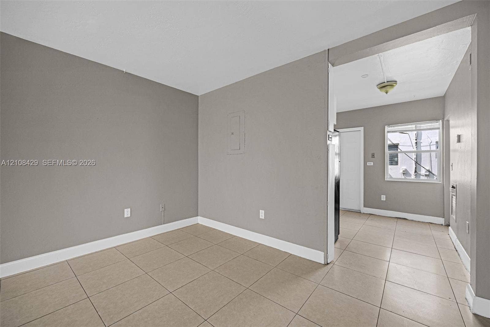 1430 NE 171st Street, North Miami Beach, FL 33162 Neutral-toned interior featuring large-format ceramic tile flooring, matte grey wall finishes, and a single-pane window with a horizontal blind