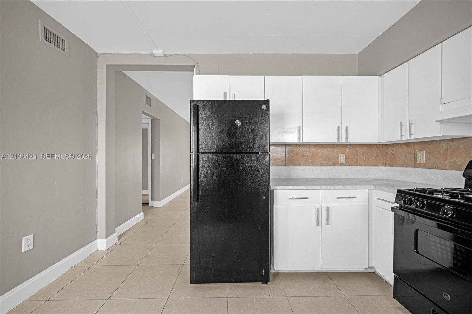 1430 NE 171st Street, North Miami Beach, FL 33162 Kitchen featuring white shaker-style cabinetry, matte black appliances, neutral tile flooring, and a stone-tiled backsplash