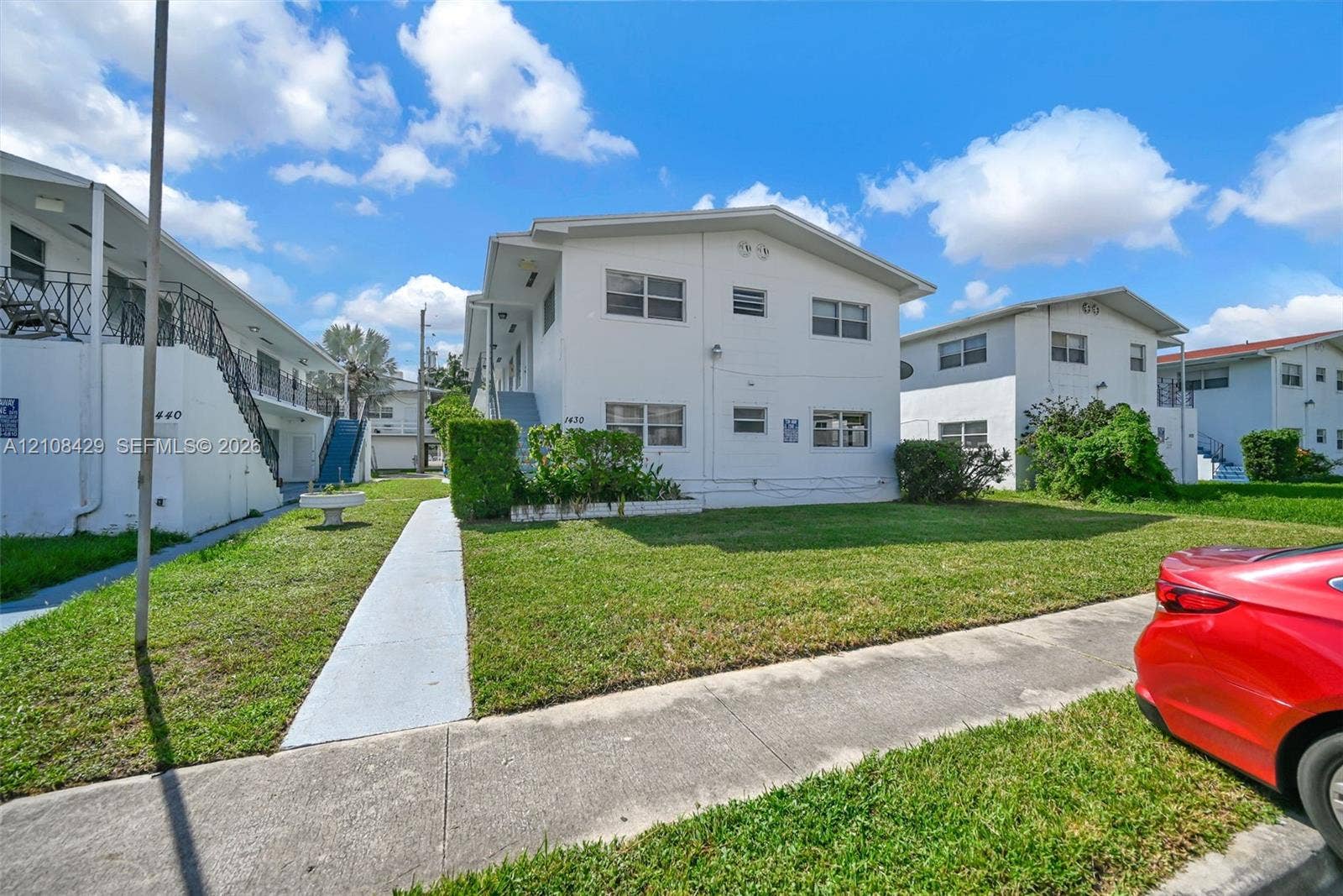1430 NE 171st Street, North Miami Beach, FL 33162 Multi-story stucco exterior featuring exterior staircases, manicured lawn, and mature landscaping