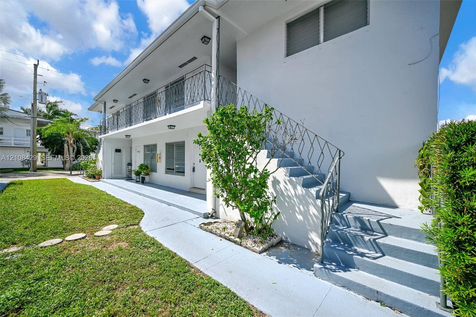 1430 NE 171st Street, North Miami Beach, FL 33162 Exterior facade featuring a painted stucco finish, wrought-iron staircase and balcony railings, covered walkway, and manicured lawn