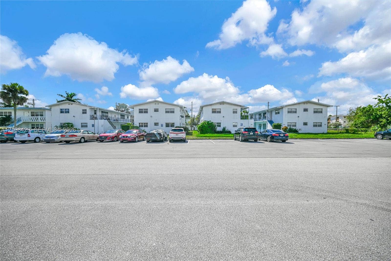 1430 NE 171st Street, North Miami Beach, FL 33162 Multi-story residential complex featuring white stucco facades, flat roofs, and dedicated asphalt surface parking