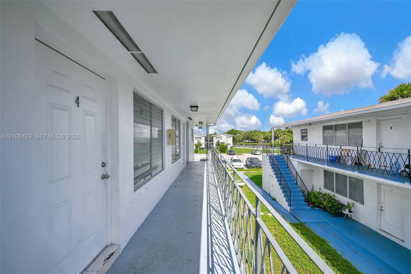 1430 NE 171st Street, North Miami Beach, FL 33162 Exterior walkway featuring white painted stucco finish, horizontal sliding windows, flush-mount ceiling lighting, and black metal railings