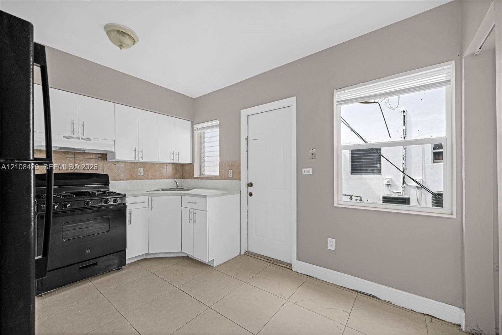 1430 NE 171st Street, North Miami Beach, FL 33162 Kitchen featuring white cabinetry, tile flooring, stone-finish backsplash, and black appliances
