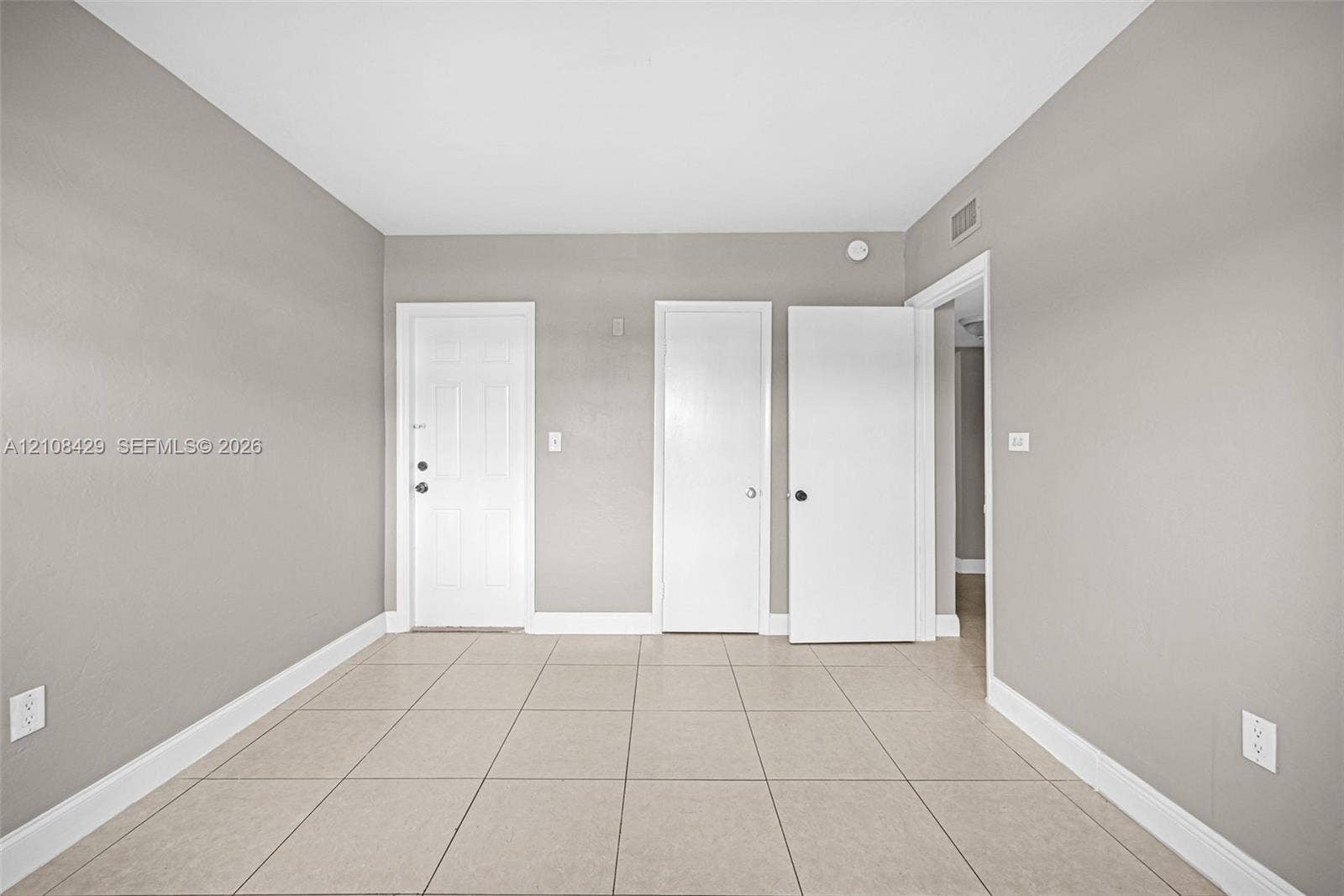 1430 NE 171st Street, North Miami Beach, FL 33162 Neutral-toned interior room featuring large-format ceramic tile flooring, three white paneled doors, and smooth, light-grey wall finishes
