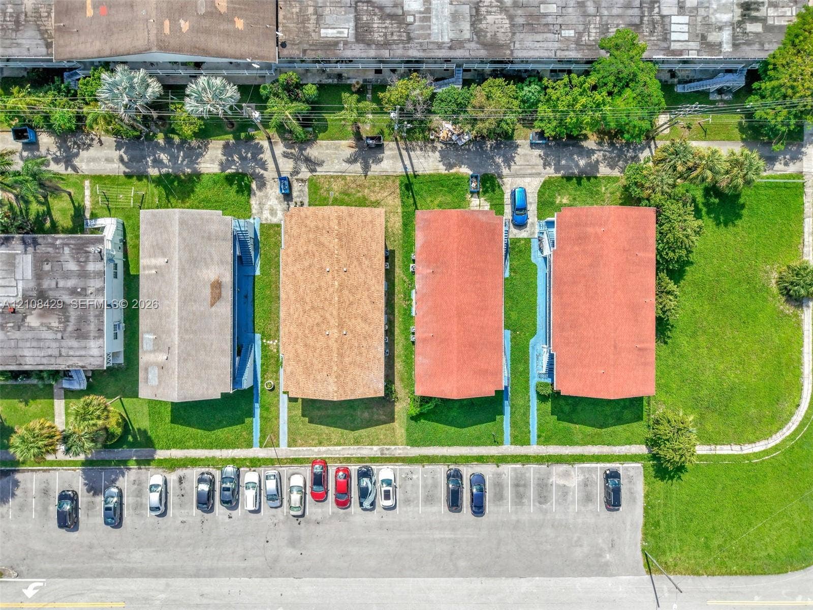 1430 NE 171st Street, North Miami Beach, FL 33162 Aerial perspective featuring multiple rectangular residential structures with gabled roofing, integrated walkways, surrounding grass landscaping, and assigned surface parking