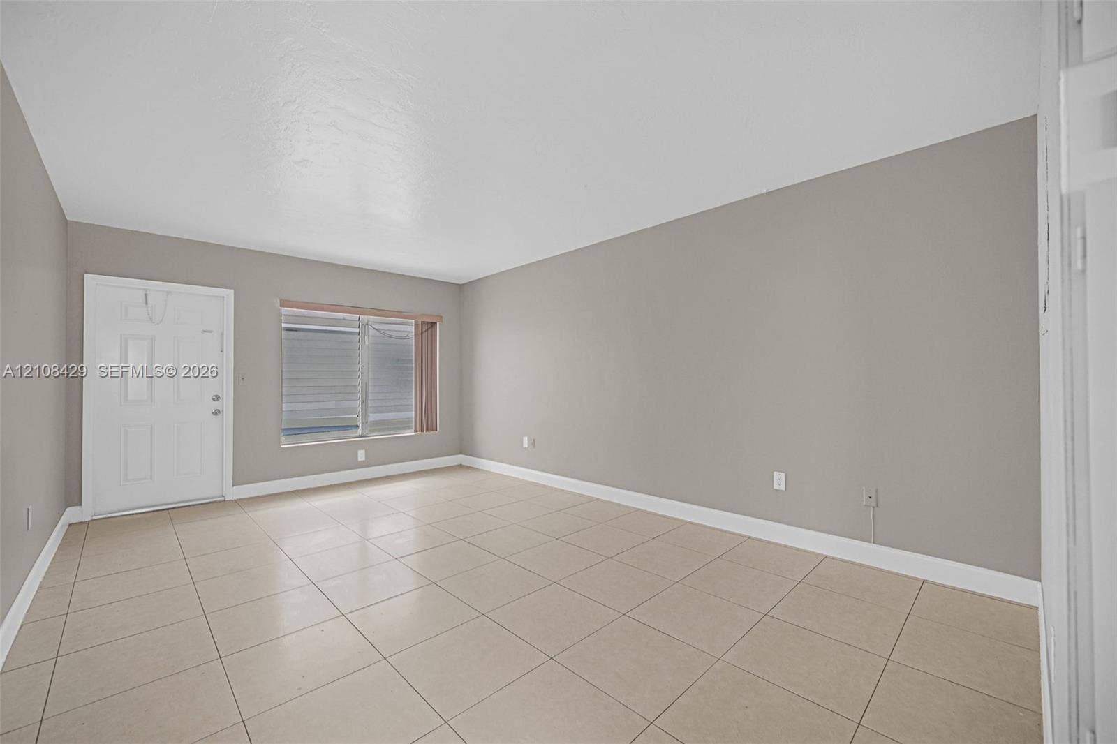 1430 NE 171st Street, North Miami Beach, FL 33162 Neutral interior featuring large-format tile flooring, light-toned wall paint, a multi-pane window, and an exterior-grade entry door