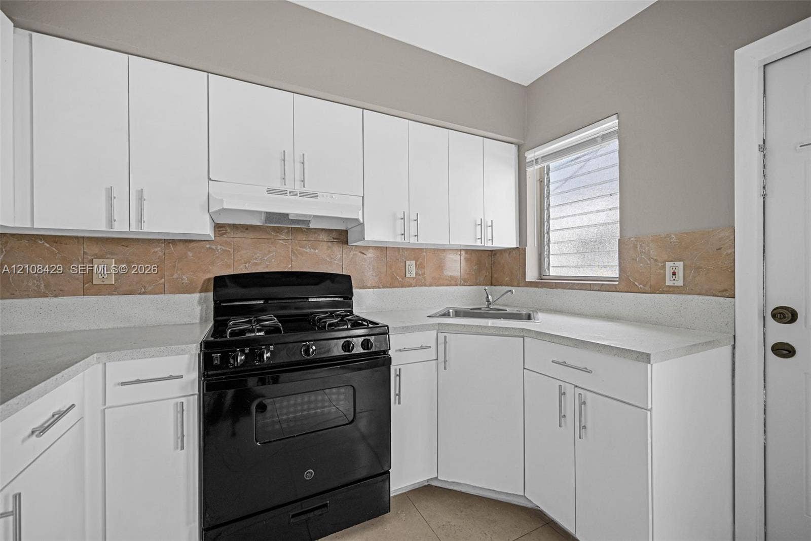 1430 NE 171st Street, North Miami Beach, FL 33162 Kitchen featuring white cabinetry, solid-surface countertops, stone-finish backsplash, and a black range