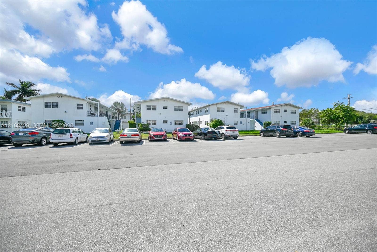 1430 NE 171st Street, North Miami Beach, FL 33162 Multi-family residential complex featuring white stucco exteriors, low-pitch roofs, and dedicated asphalt surface parking