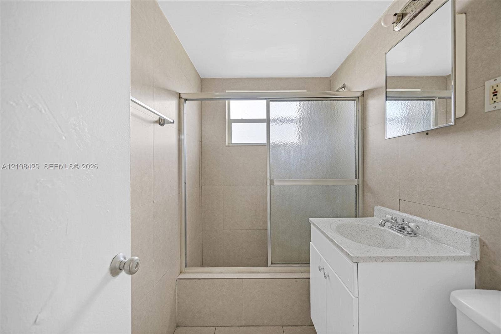 1430 NE 171st Street, North Miami Beach, FL 33162 Bathroom featuring a shower-tub combination with sliding glass doors, neutral tile wall surround, white vanity with a composite countertop, and an integrated mirrored medicine cabinet