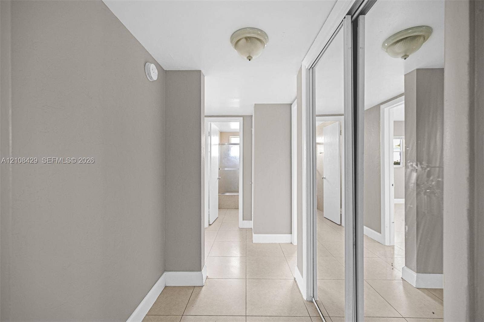 1430 NE 171st Street, North Miami Beach, FL 33162 Hallway featuring tile flooring, sliding mirror-panel closet doors, and flush-mount ceiling light fixtures