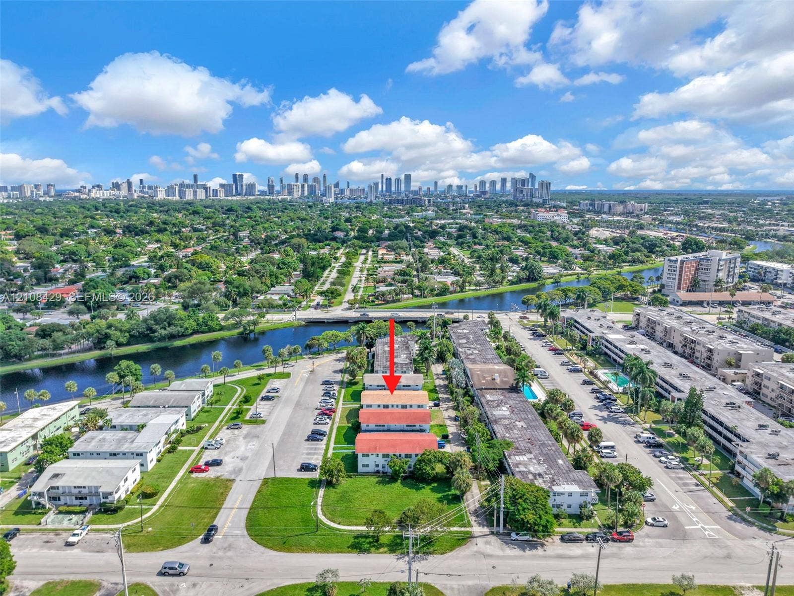 1430 NE 171st Street, North Miami Beach, FL 33162 Aerial perspective featuring a multi-unit residential building with a red tile roof, surrounded by green space, paved parking, and a canal