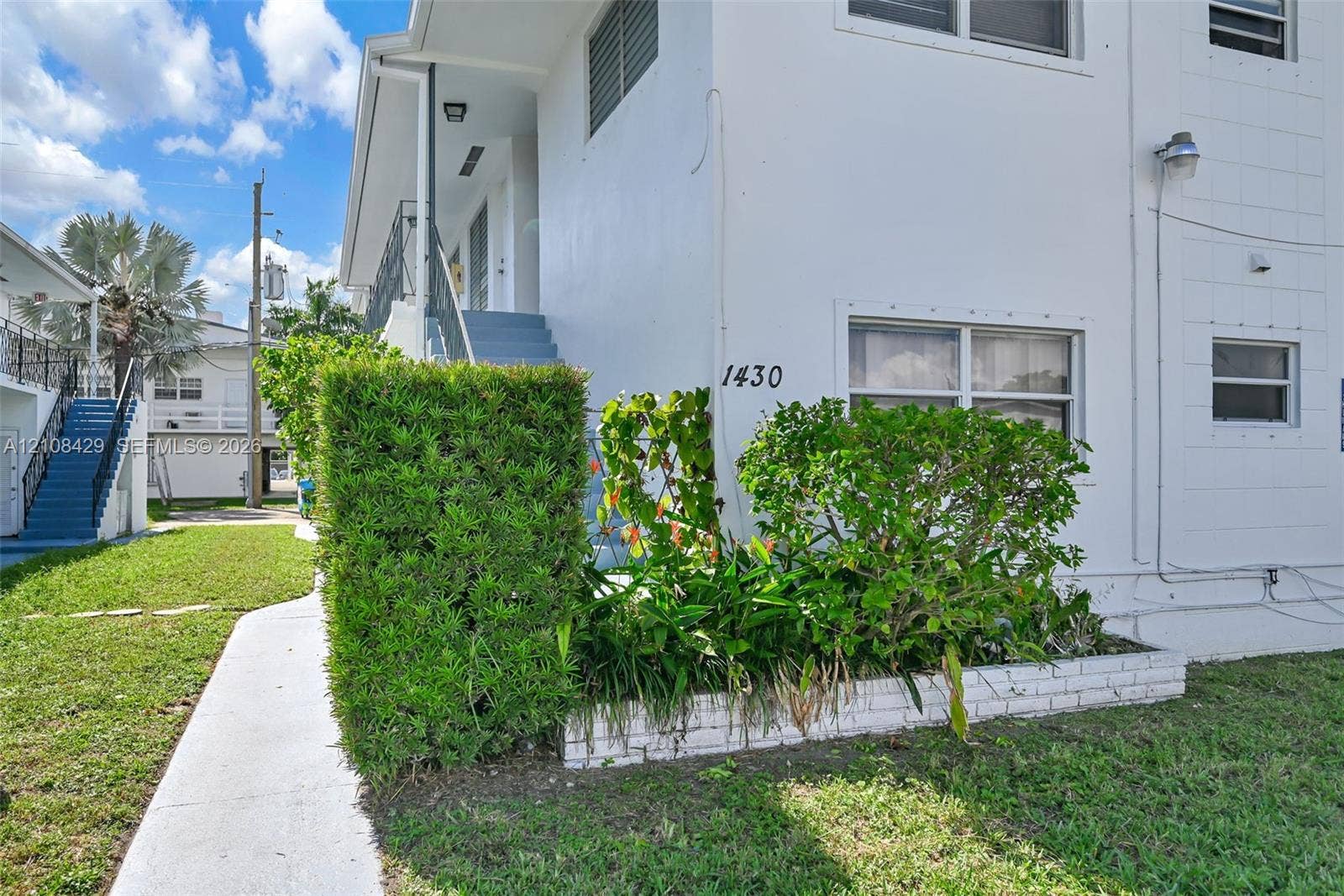 1430 NE 171st Street, North Miami Beach, FL 33162 Stucco exterior featuring multi-level metal railings, integrated landscaping, white brick planter boxes, and concrete walkways
