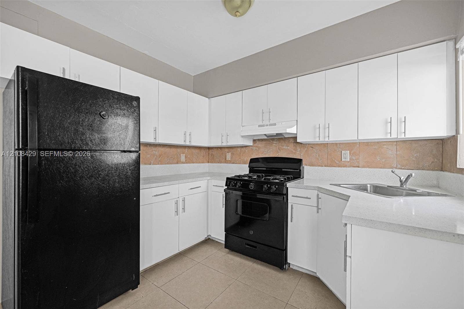 1430 NE 171st Street, North Miami Beach, FL 33162 Kitchen featuring white shaker-style cabinetry, solid-surface countertops, tile backsplash, tile flooring, and black appliance suite