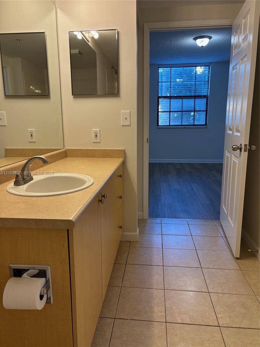 1919 Van Buren Street, #219A, Hollywood, FL 33020 Bathroom featuring a laminate countertop, integrated sink with a curved faucet, light wood-finish cabinetry, ceramic tile flooring, and a flat-panel mirror