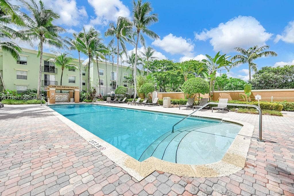 1919 Van Buren Street, #219A, Hollywood, FL 33020 Swimming pool with stepped entry, surrounding brick paver deck, and lush tropical landscaping