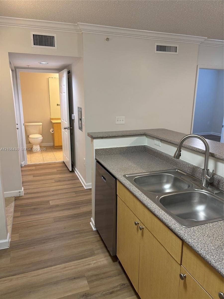 1919 Van Buren Street, #219A, Hollywood, FL 33020 Kitchen featuring a dual-basin stainless steel sink, gooseneck faucet, integrated dishwasher, solid-surface countertops, and wood-finish flooring