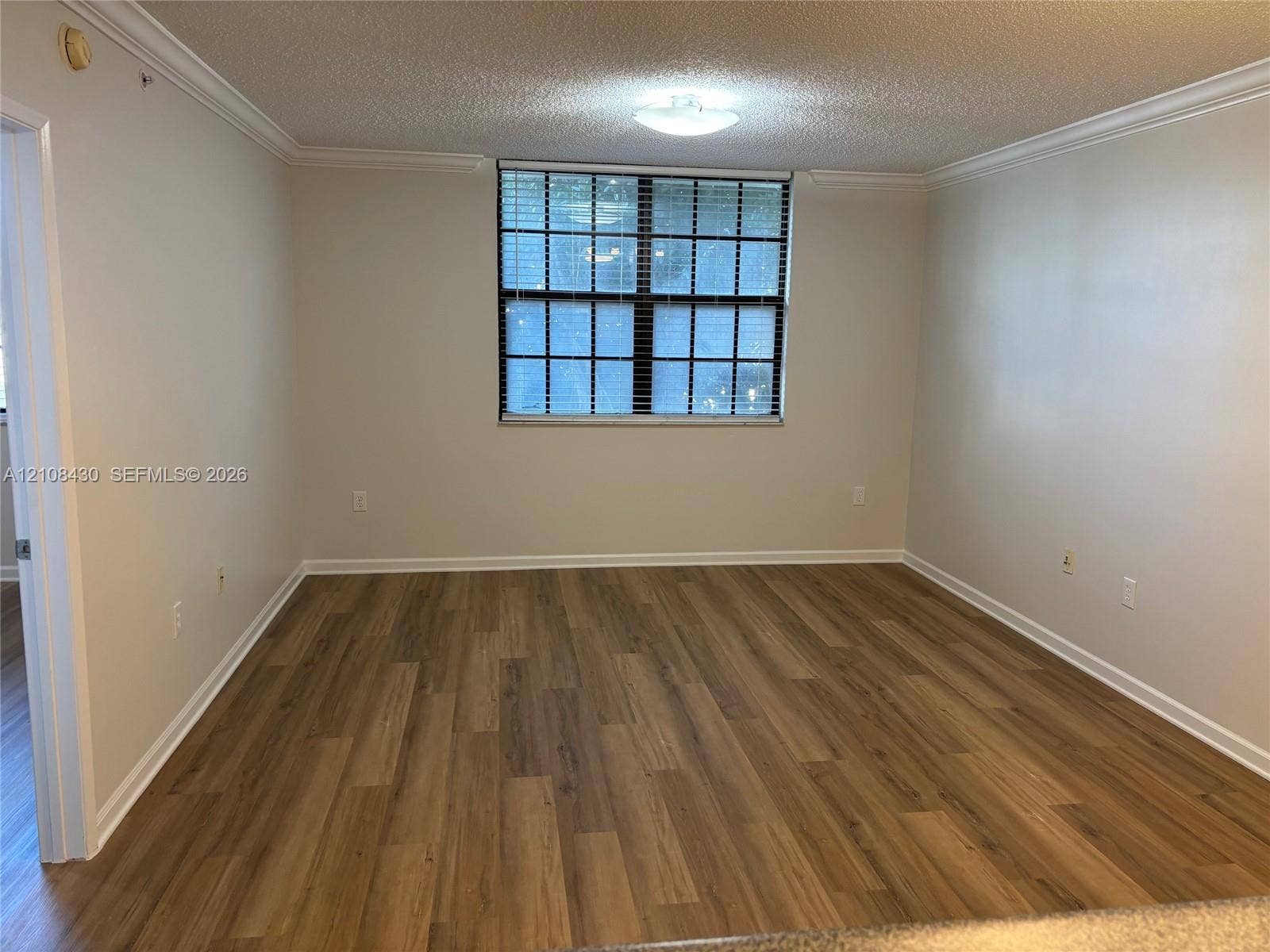 1919 Van Buren Street, #219A, Hollywood, FL 33020 Room interior featuring wood-finish flooring, neutral wall tones, multi-pane window with horizontal blinds, and crown molding