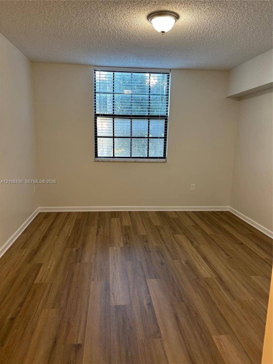 1919 Van Buren Street, #219A, Hollywood, FL 33020 Room featuring wood-finish flooring, a multi-pane window with integrated blinds, and a flush-mount ceiling light fixture