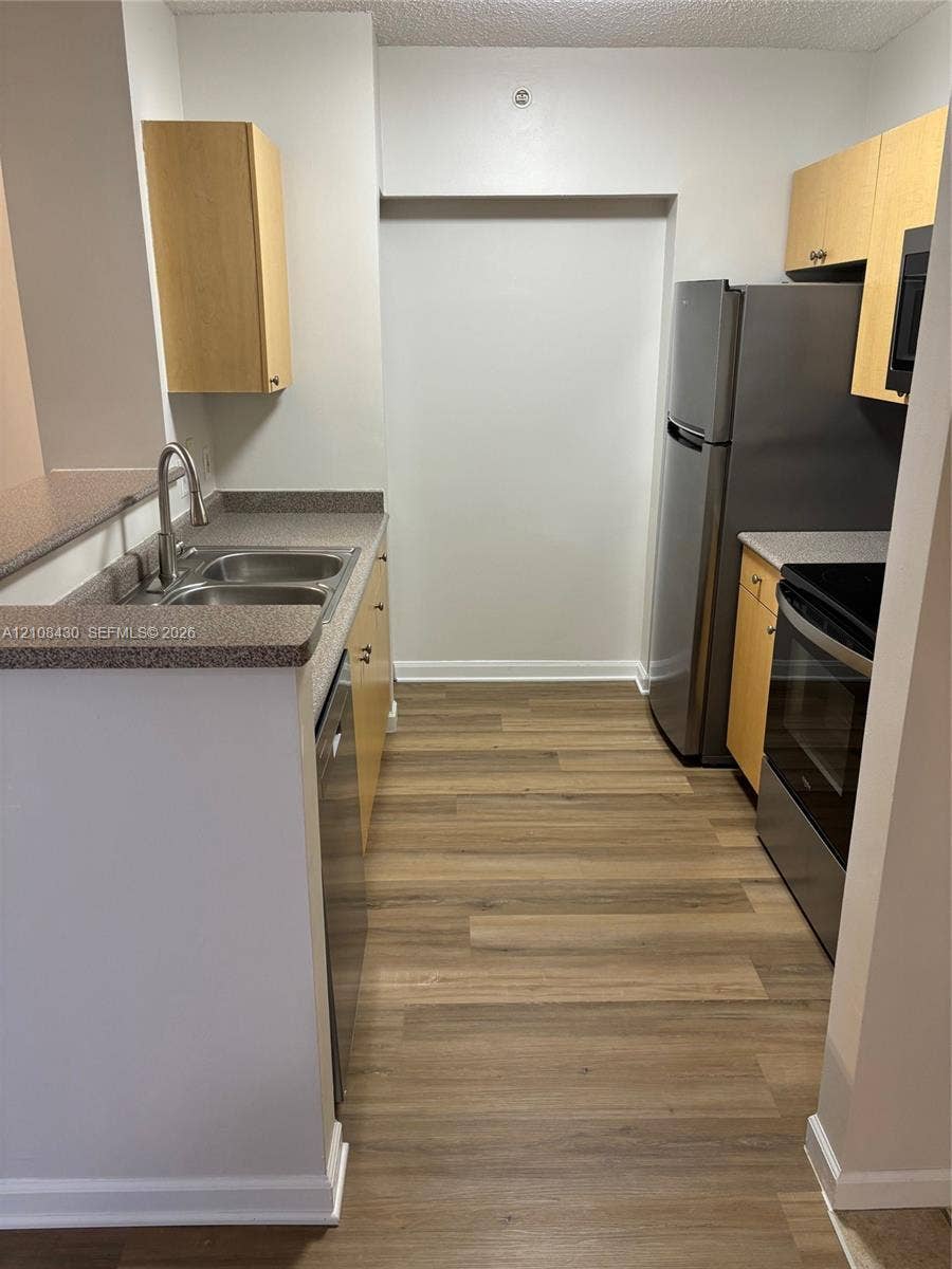 1919 Van Buren Street, #219A, Hollywood, FL 33020 Kitchen featuring wood-finish cabinetry, stone-texture countertops, stainless steel appliances, wood-finish flooring, and a dual-basin sink with a pull-down faucet