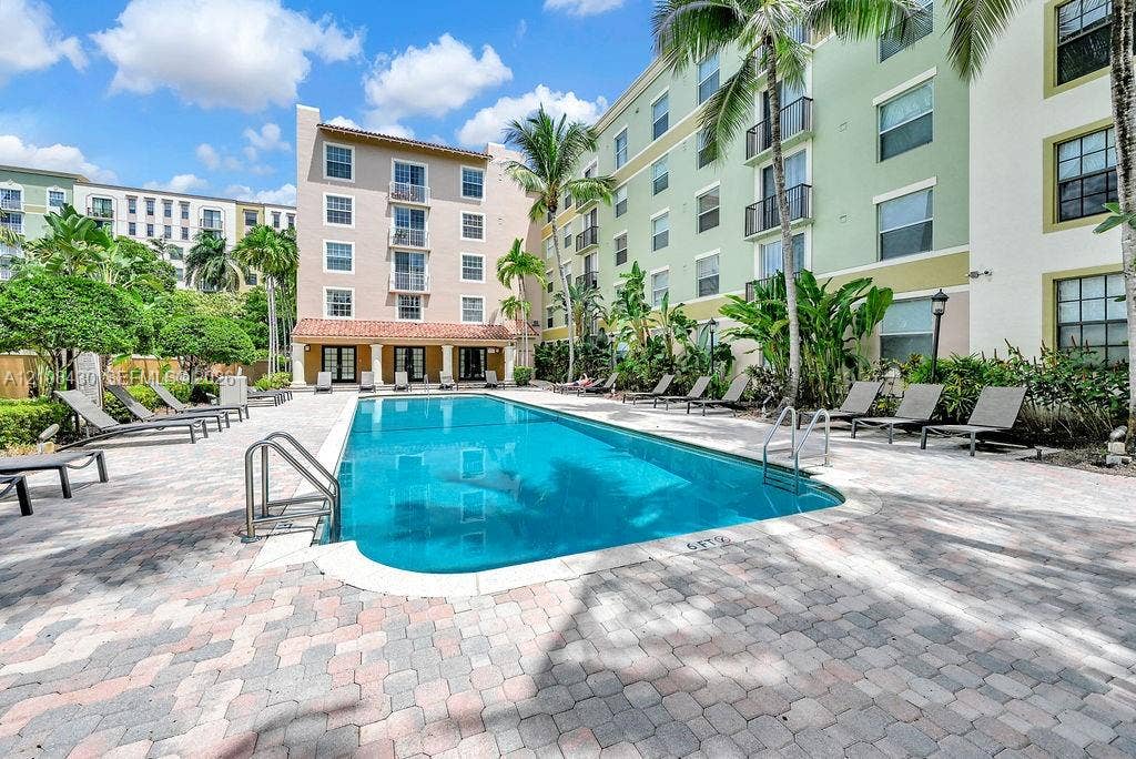 1919 Van Buren Street, #219A, Hollywood, FL 33020 In-ground pool with metal handrails, surround finished in stone pavers, and landscaped grounds featuring mature palms