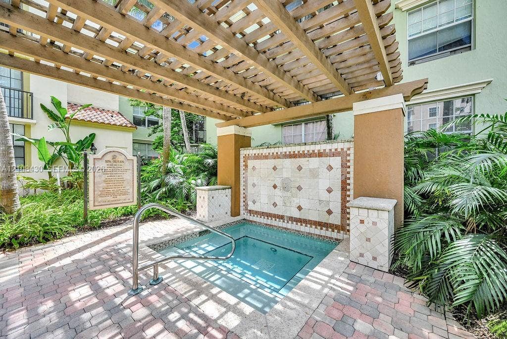 1919 Van Buren Street, #219A, Hollywood, FL 33020 Spa area featuring a stone-tiled accent wall, overhead wooden pergola, brick paver decking, and metal handrail