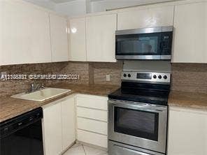 100 Bayview Drive, #1904, Sunny Isles Beach, Sunny Isles Beach, FL 33160 Kitchen featuring high-gloss white cabinetry, stone-finish countertops, tiled backsplash, and stainless steel appliances including a built-in microwave and range