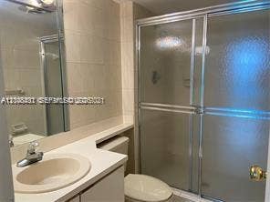 100 Bayview Drive, #1904, Sunny Isles Beach, Sunny Isles Beach, FL 33160 Bathroom featuring a solid-surface vanity countertop with an integrated basin, chrome-finish faucet, full-width vanity mirror, and a walk-in shower enclosure with sliding glass doors and tiled surround