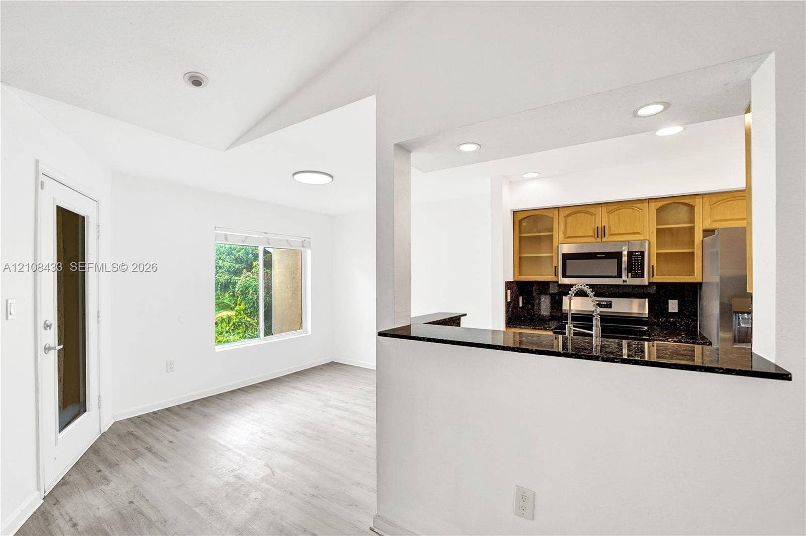 2300 NW 33rd Street, #911, Oakland Park, FL 33309 Kitchen featuring wood-finish cabinetry, stone-surface counters, and built-in stainless steel appliances, accented by wood-finish flooring, vaulted ceilings, and recessed lighting