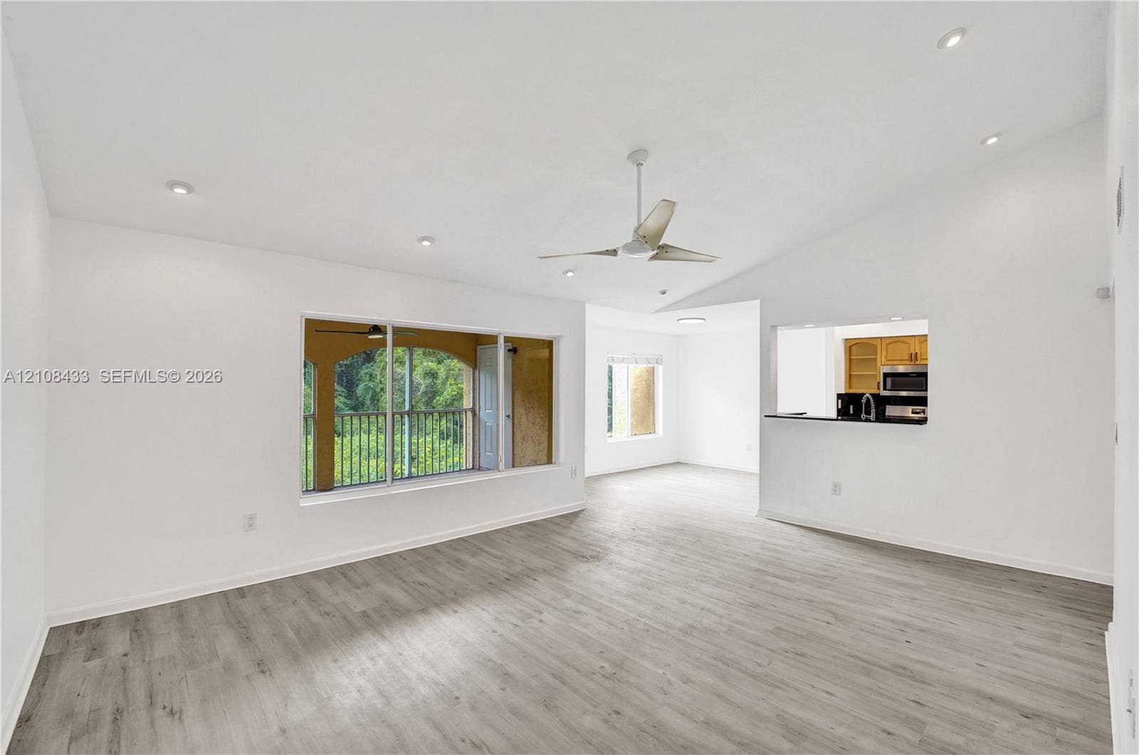 2300 NW 33rd Street, #911, Oakland Park, FL 33309 Open living area featuring vaulted ceilings, wood-finish flooring, recessed lighting, a ceiling fan, and a pass-through opening to the kitchen