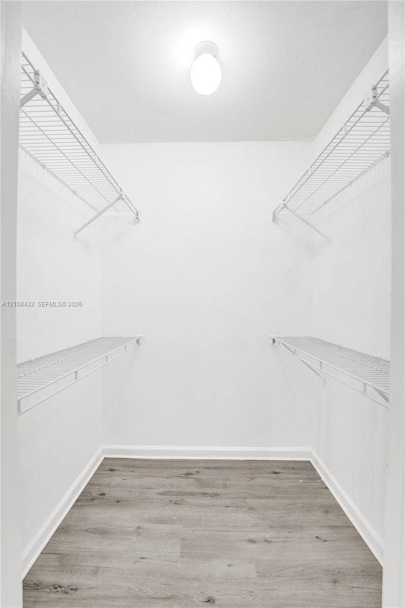 2300 NW 33rd Street, #911, Oakland Park, FL 33309 Walk-in closet featuring dual-level white wire shelving, flush-mount dome lighting, and wood-finish flooring