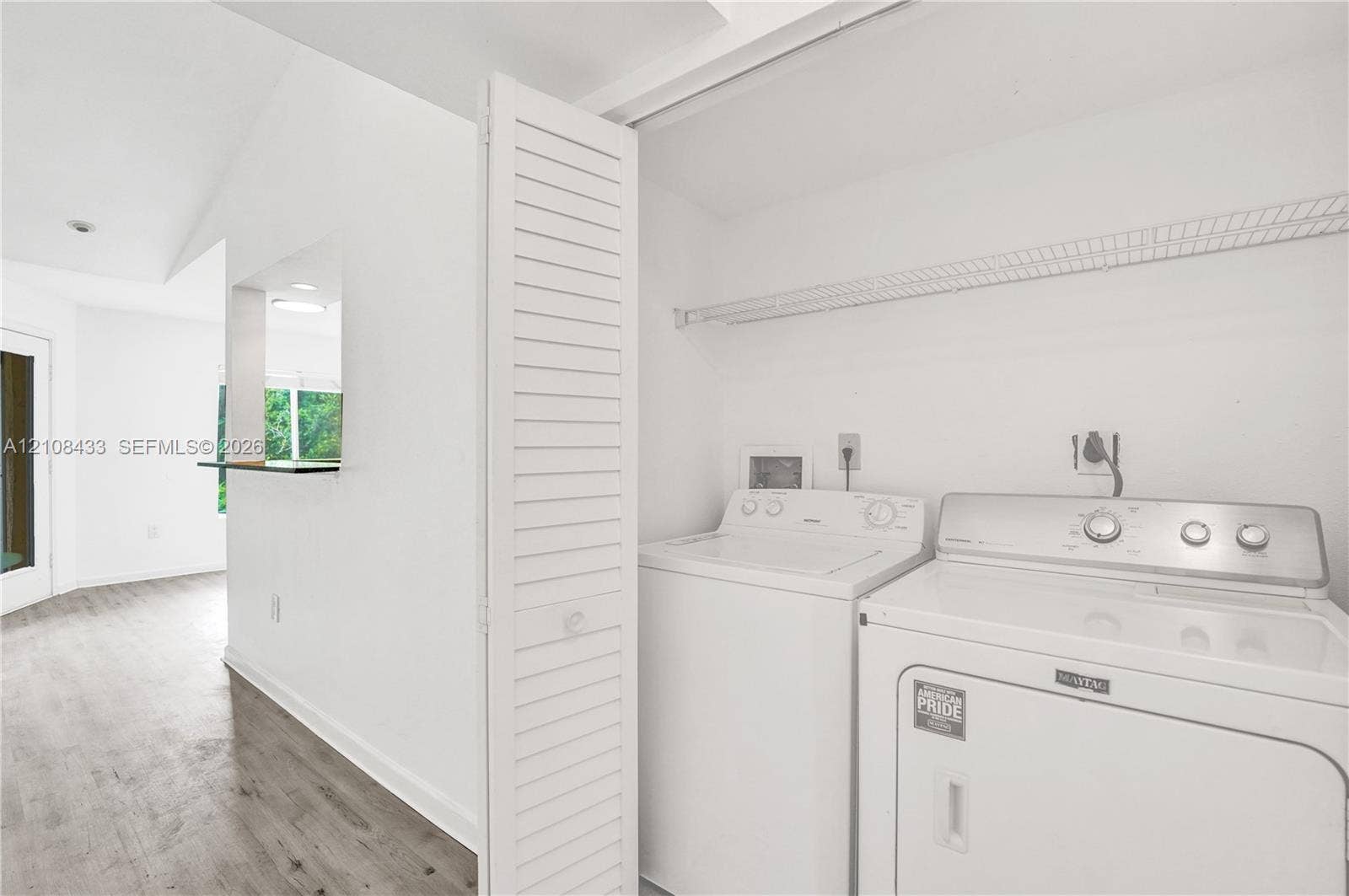 2300 NW 33rd Street, #911, Oakland Park, FL 33309 Laundry closet featuring louvered bi-fold doors, overhead wire shelving, and wood-finish flooring