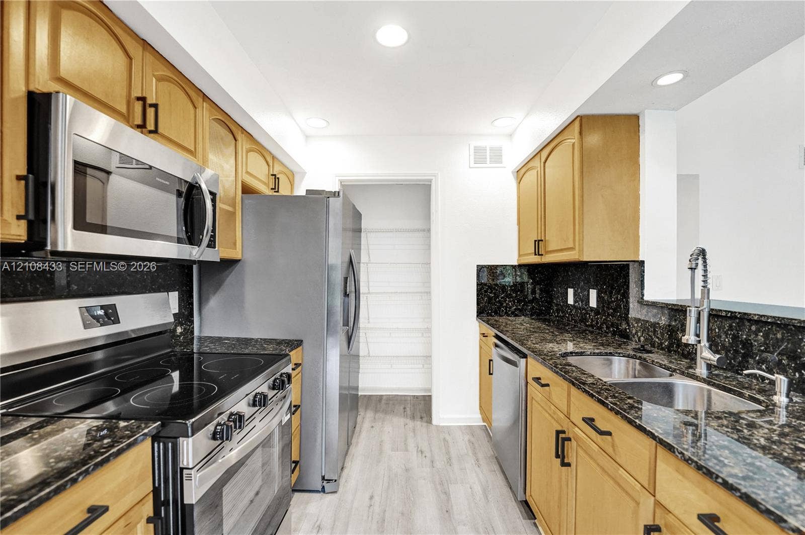 2300 NW 33rd Street, #911, Oakland Park, FL 33309 Kitchen featuring natural finish cabinetry, dark stone countertops, stainless steel appliances, a pull-down kitchen faucet, and wood-finish flooring
